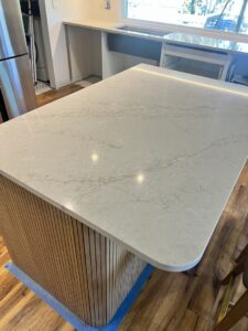 A close-up of a newly installed kitchen island countertop with a light patterned surface and a modern wood slat base by AAA Countertops in Austin, TX.