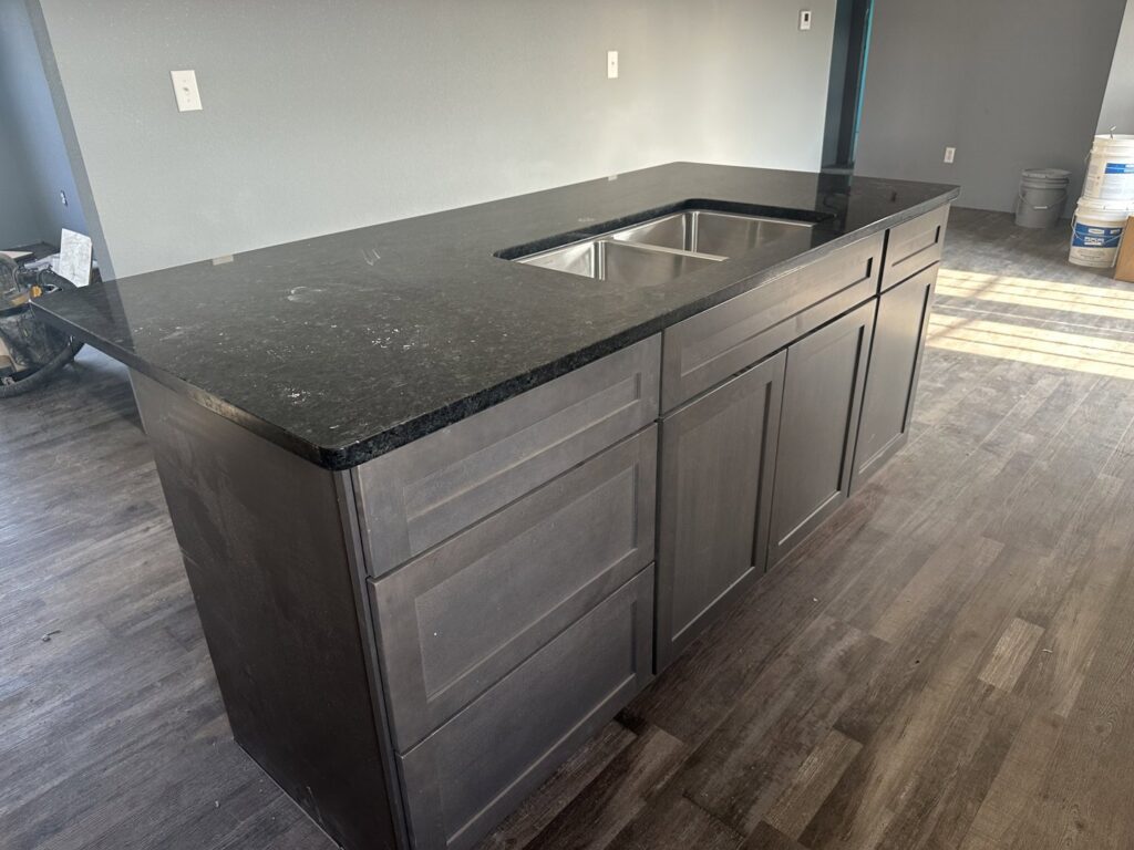 A kitchen island with dark cabinets and sleek black countertops, featuring a double sink, installed by Javier's Countertops in Springdale, AR