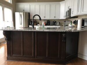 A kitchen island with dark wood paneling and a white granite countertop, part of a project by Cincinnati Cabinet Refacing in Cincinnati, OH.