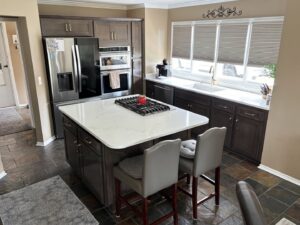A spacious kitchen with dark wood cabinets, a large island with a gas cooktop, and a white farmhouse sink by Creative Building & Remodeling in Warren, MI