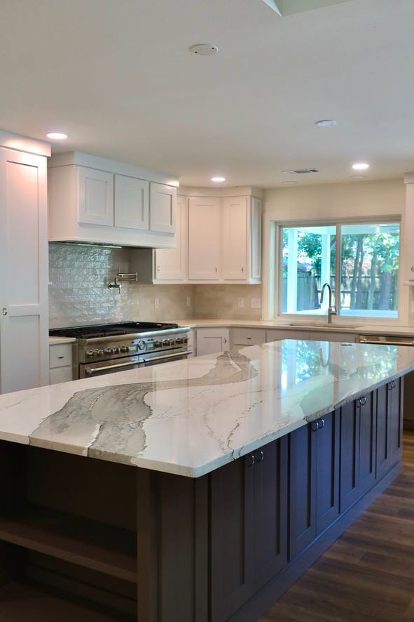 A renovated kitchen featuring a large island with a unique countertop and a professional range by Holaway Custom Builds in Fayetteville, AR.