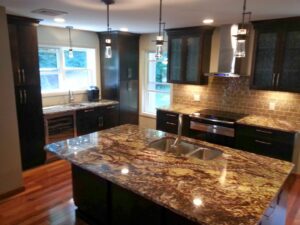 A renovated kitchen featuring dark cabinets, a large island with a sink, and light countertops by Mainville Construction & Remodeling LLC in Newington, CT.