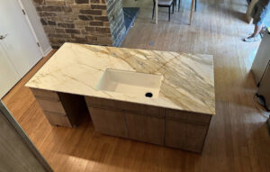 A kitchen island featuring a light-colored, heavily veined countertop with an undermount sink installed by Javier's Countertops in Springdale, AR