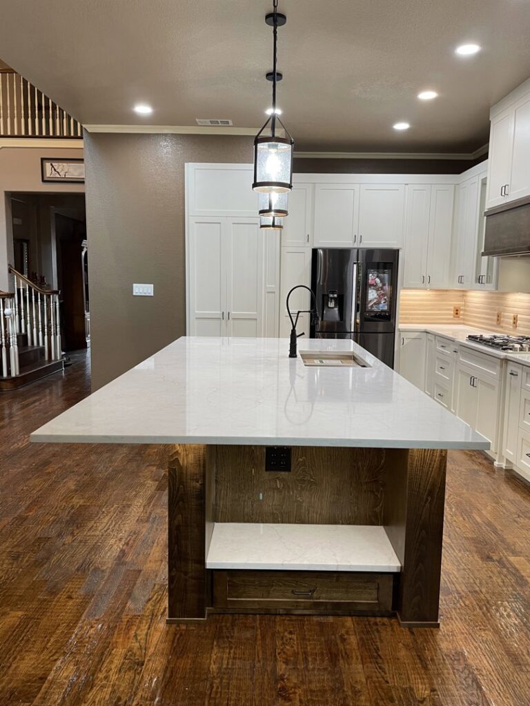 A stylish kitchen island with a white countertop and dark wood base, illuminated by pendant lights, a remodel by Whole House Remodel & Design North Dallas Tx in Frisco, TX.