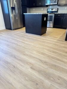 A modern kitchen featuring light wood-look laminate flooring, black cabinets, and stainless steel appliances installed by SD Masters in Miami, FL.