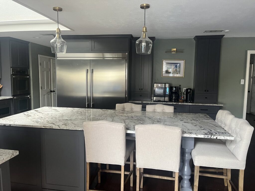 A renovated kitchen featuring a large island with granite countertops, dark grey cabinets, and stainless steel appliances by Whole House Remodel & Design North Dallas Tx in Frisco, TX.
