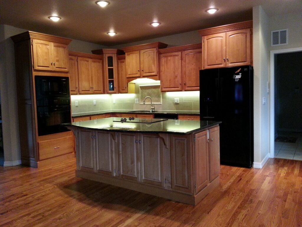 A remodeled kitchen featuring light wood cabinets, black appliances, and under-cabinet lighting by Advanced Remodeling Services in Elbert, CO.