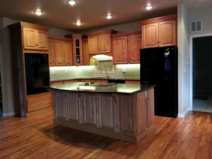 A remodeled kitchen featuring light wood cabinets, black appliances, and under-cabinet lighting by Advanced Remodeling Services in Elbert, CO.