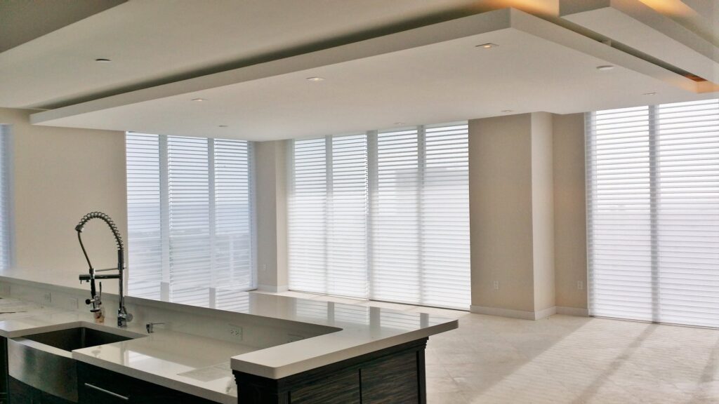 A spacious kitchen and living area featuring a large island, modern ceiling design with recessed lighting, and expansive windows, remodeled by JNY Remodeling INC in Fort Lauderdale, FL.