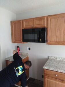A handyman installing a new microwave oven above kitchen cabinets for Holy City Remodel in North Charleston, SC.