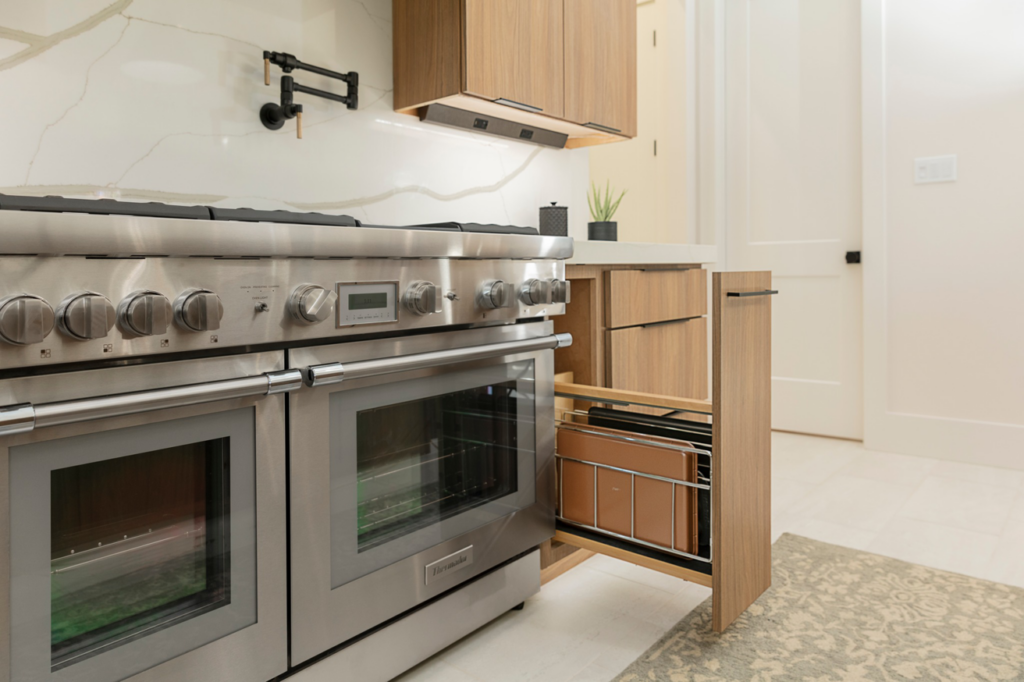 Close-up of a stainless steel kitchen range and a custom pull-out baking sheet organizer by Preferred Millworks & Design in Edmond, OK.