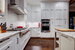A modern kitchen range, stainless steel hood, and built-in ovens in a renovation by Adams Company in Cedar Park, TX