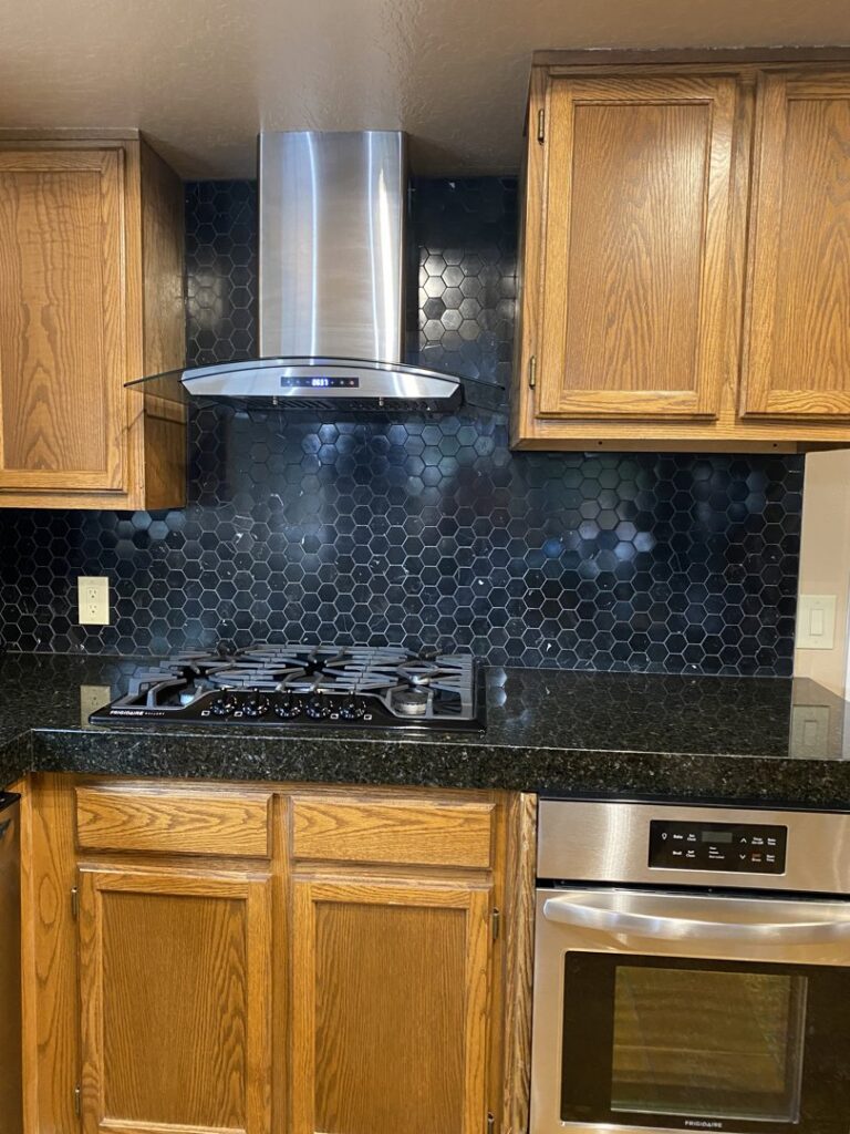 A kitchen featuring a newly installed stainless steel range hood and black hexagonal tile backsplash by Prospective 1, LLC in Sparks, NV.