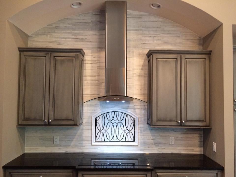 A kitchen remodel featuring a stylish range hood, custom cabinets, and decorative tile backsplash by Pro Remodel LLC in St. Charles, MO.
