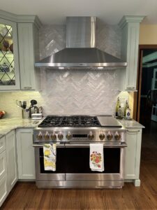 A kitchen remodel showcasing a large professional range, stainless steel hood, and light green cabinets by Synergy Builders in West Chicago, IL.