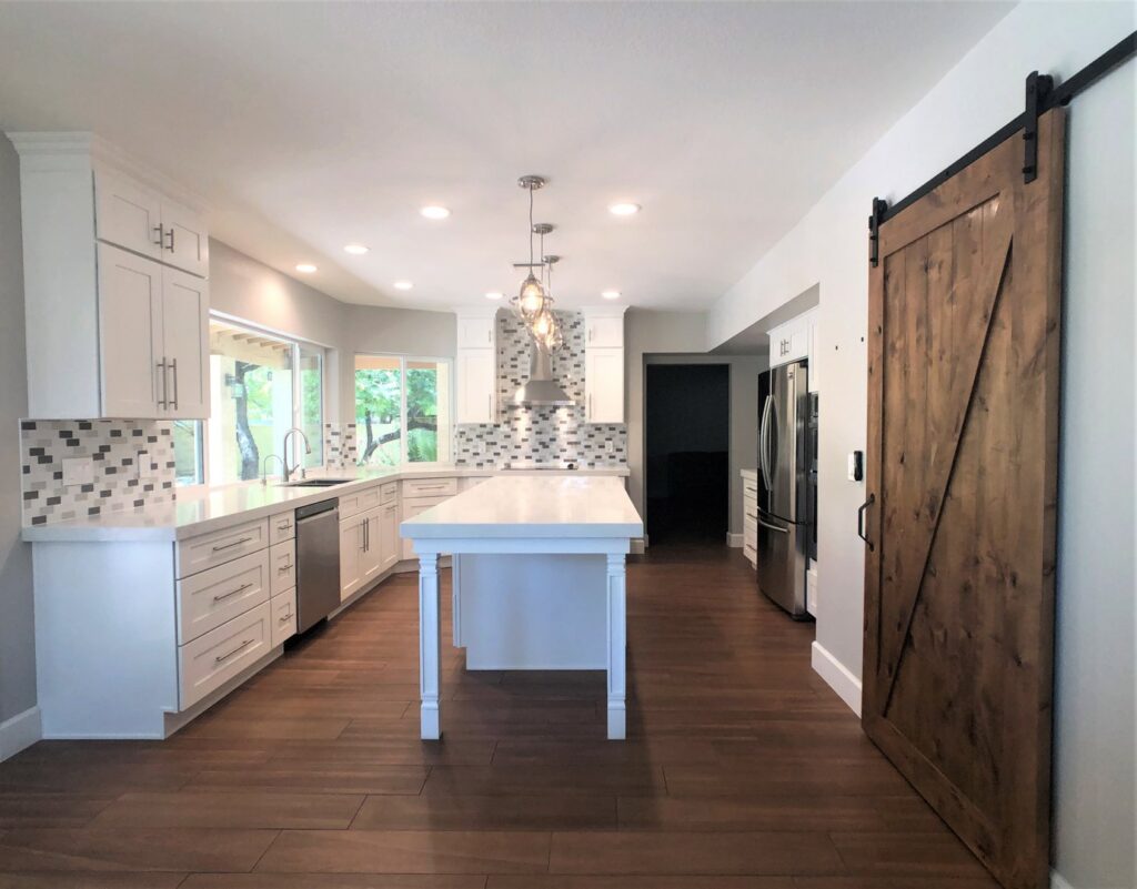 A spacious kitchen remodel featuring white cabinets, a large island, and a stylish barn door by Ignite Construction in Tempe, AZ.