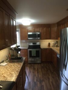 A renovated kitchen with rich brown cabinets, stainless steel appliances, and wood-look flooring by Pink Rose Home Service in Rochester, NY.