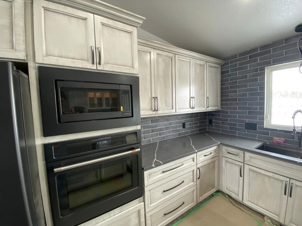 A renovated kitchen with white cabinets, dark subway tile backsplash, and built-in appliances by Vander Wal Contracting, LLC in Bismarck, ND