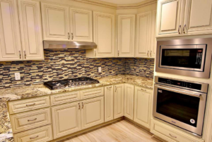 A beautifully remodeled kitchen featuring cream cabinets, granite countertops, and a mosaic tile backsplash by Regal Remodelers in Baton Rouge, LA.