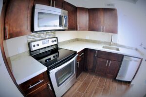 A completed kitchen remodel featuring dark wood cabinets, stainless steel appliances, and a stylish tiled backsplash by JNY Remodeling INC in Fort Lauderdale, FL.