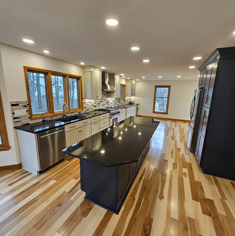 A kitchen remodel featuring a dark island, white cabinets, and light wood flooring by Antalek Construction LLC in Erie, PA