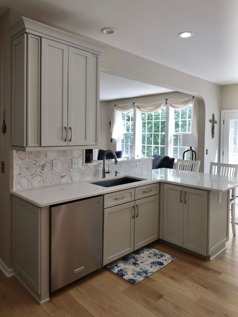 A kitchen remodel featuring light grey cabinets, white countertop, and a new sink and dishwasher installation by The Bath Shop in Raleigh, NC.