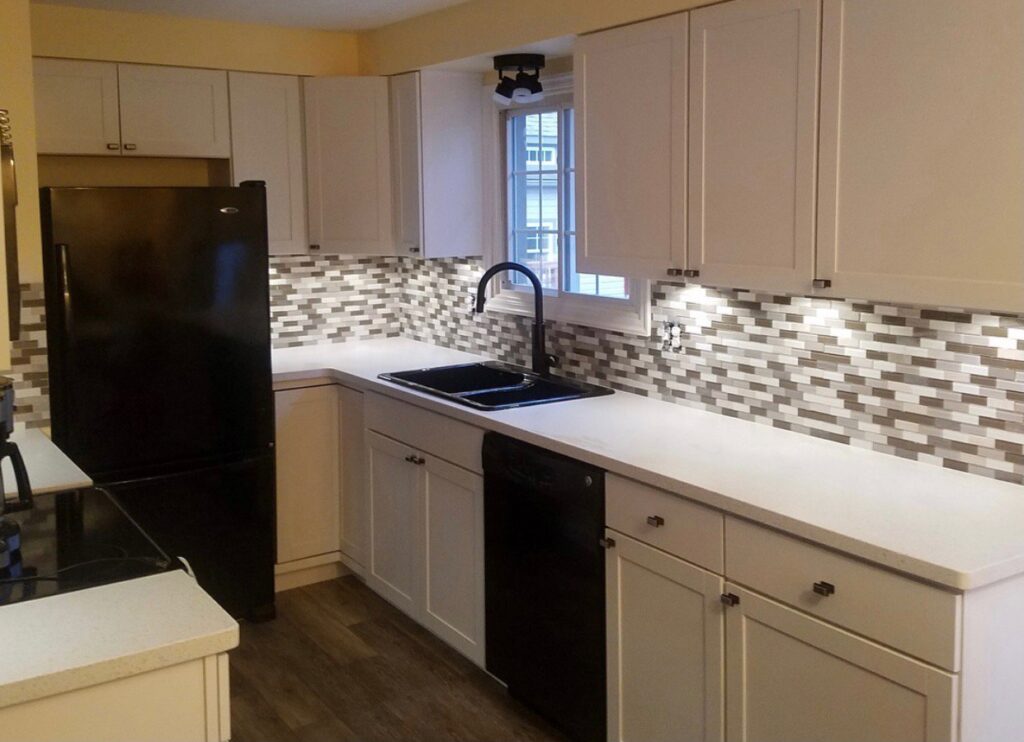 A completed kitchen remodel with white cabinets, dark appliances, and a stylish mosaic tile backsplash by Rock Solid Construction in Rochester, NY