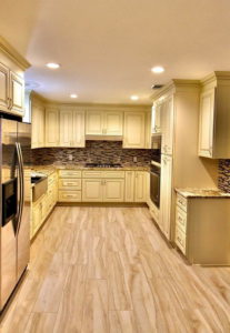 A remodeled kitchen with cream-colored cabinets, new wood-look tile flooring, and a mosaic backsplash by Regal Remodelers in Baton Rouge, LA.