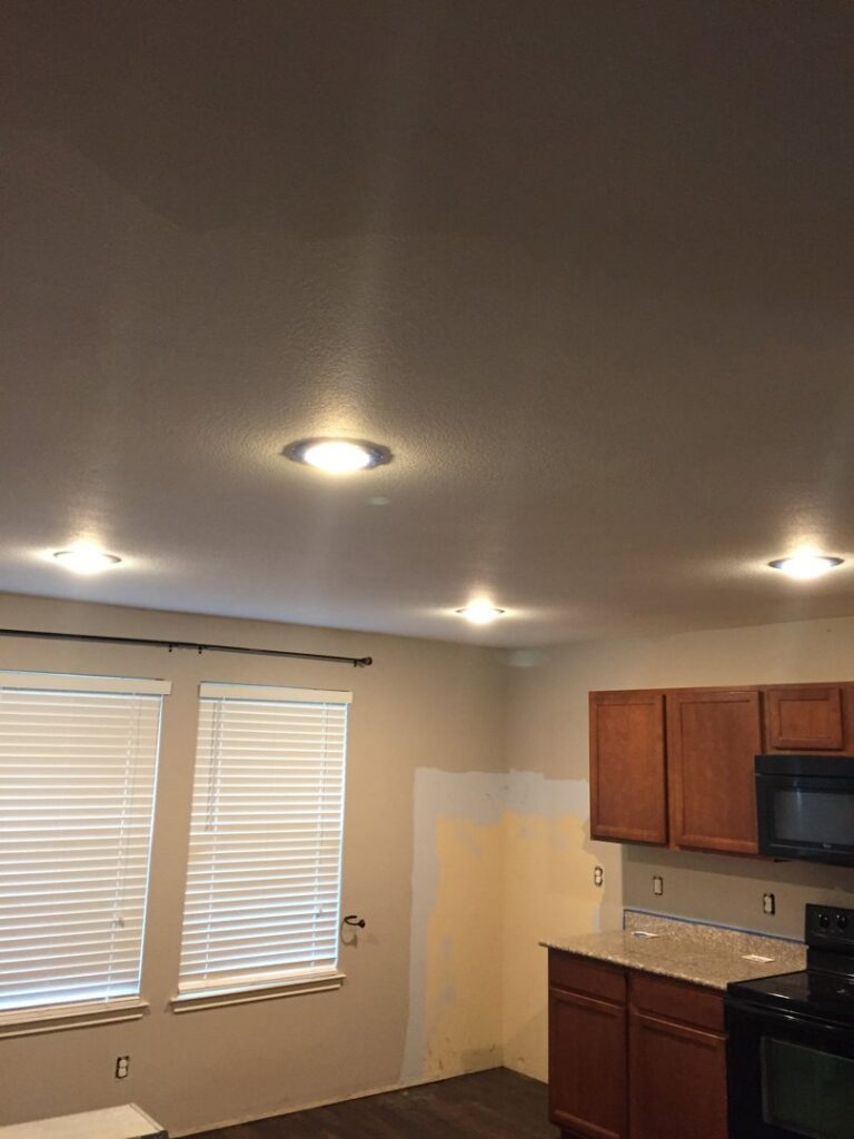 An interior view of a kitchen remodel featuring new recessed lighting, wooden cabinets, and a countertop, by Texas Wounded Veterans Builders and Contractors in McKinney, TX.