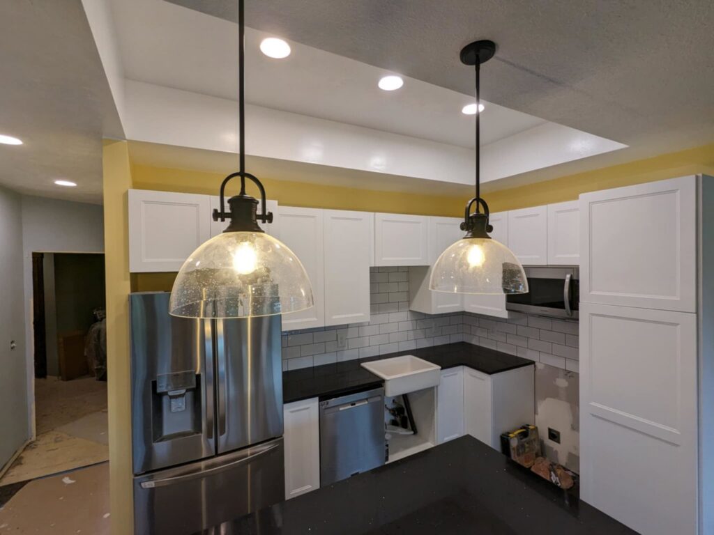 A kitchen remodel in progress with new white cabinets, black countertops, and pendant lights by Halpin Hands in Williams, OR.