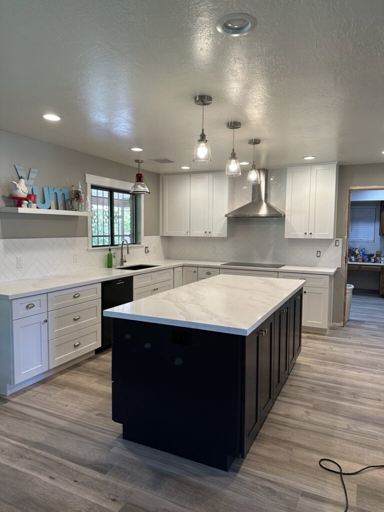 A newly remodeled kitchen featuring white upper cabinets, dark lower cabinets, and a large island with pendant lights by American Wolf Construction in Mesa, AZ