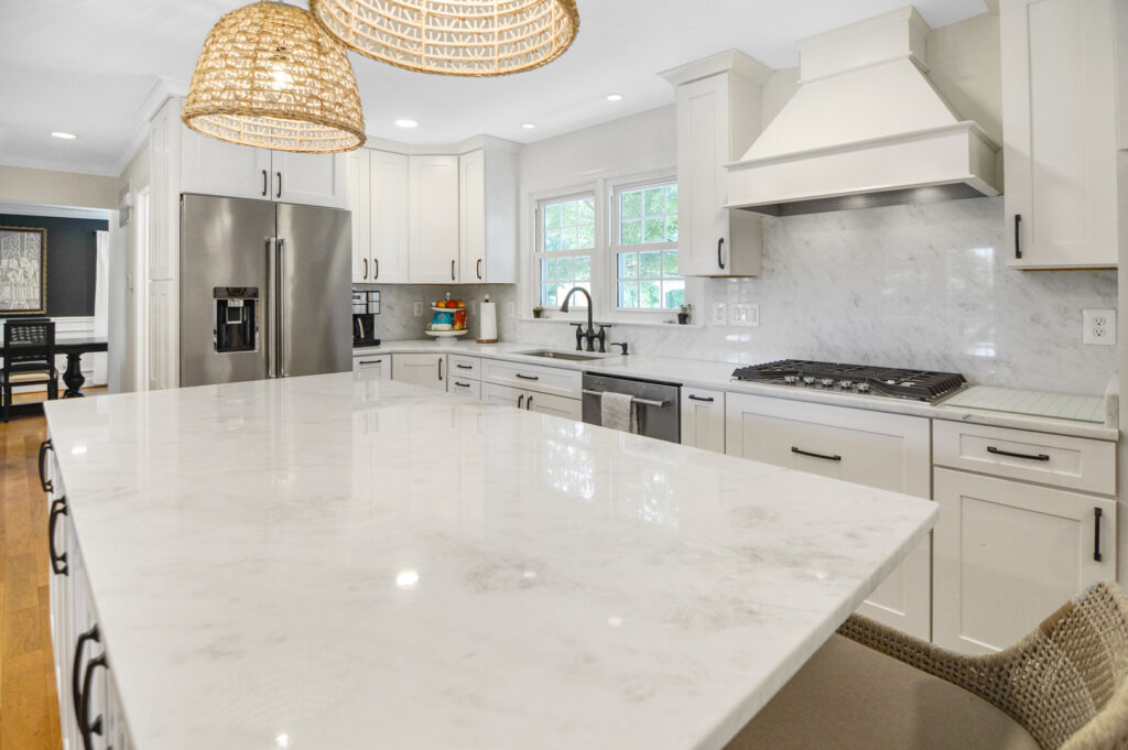 A kitchen remodel with white cabinets, a large white island, and decorative pendant lights by Total Craftsmen in Towson, MD