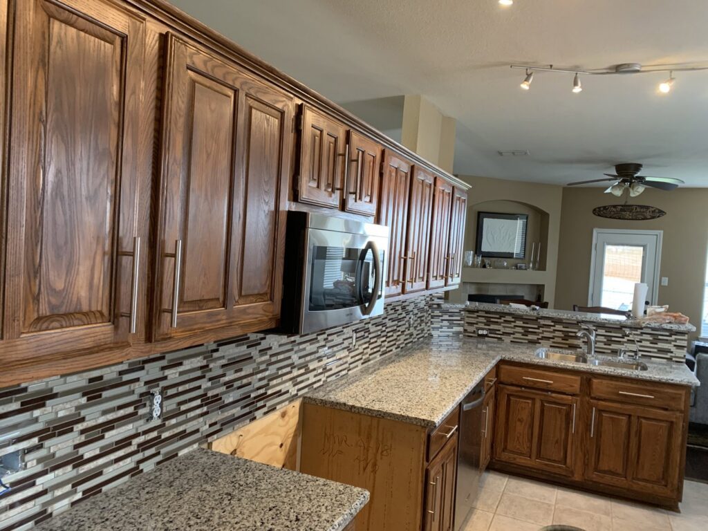 A completed kitchen remodel showcasing wooden cabinets, granite countertops, and a tiled backsplash by Brewer Builds in Fort Worth, TX.
