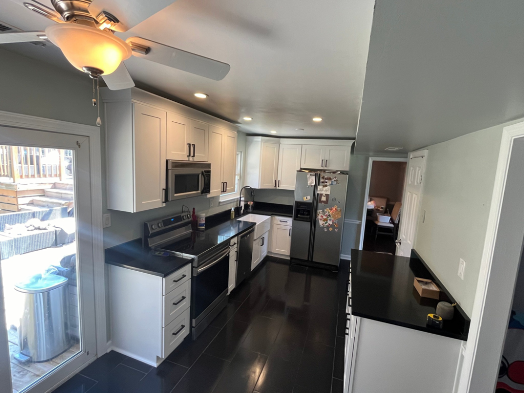 A renovated kitchen with black tile flooring, white cabinets, and new appliances by Precision Home Improvement in Massapequa, NY.