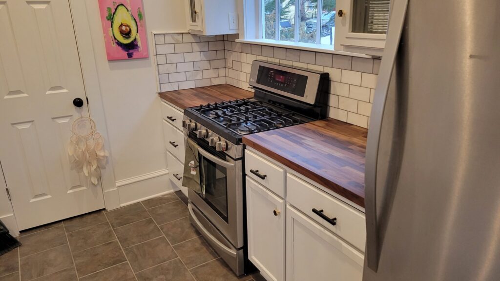 A renovated kitchen featuring white cabinets, subway tile backsplash, and warm butcher block countertops by KB Home Repairs & Improvements, LLC in Shawnee, KS.