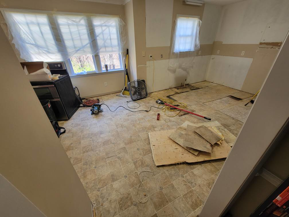 A kitchen undergoing demolition and renovation, showing removed flooring and tools, by Raleigh Renovations & Flooring in Cary, NC.