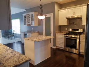 A renovated kitchen with white cabinets, granite island, and stainless steel stove by Land Bank Builders and Associates in Gary, IN