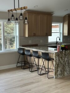 A kitchen renovation in progress, showing new light wood flooring, an island with a granite countertop, and modern light fixtures by Keeler Construction Group Inc. in Blue Island, IL.