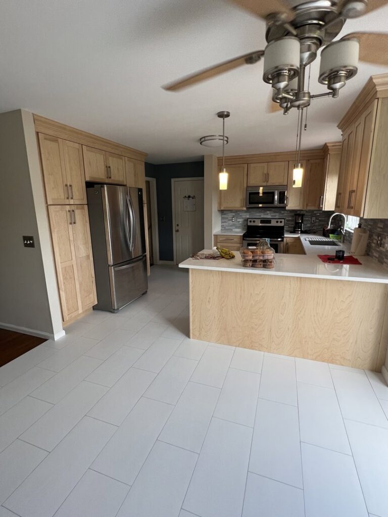 A kitchen renovation showcasing light wood cabinets, white tiled flooring, and stainless steel appliances by Amaro home improvement llc in Danbury, CT.