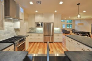 A kitchen renovation with white cabinets, stainless steel appliances, and dark countertops by Stone Age Granite of Austin, TX.