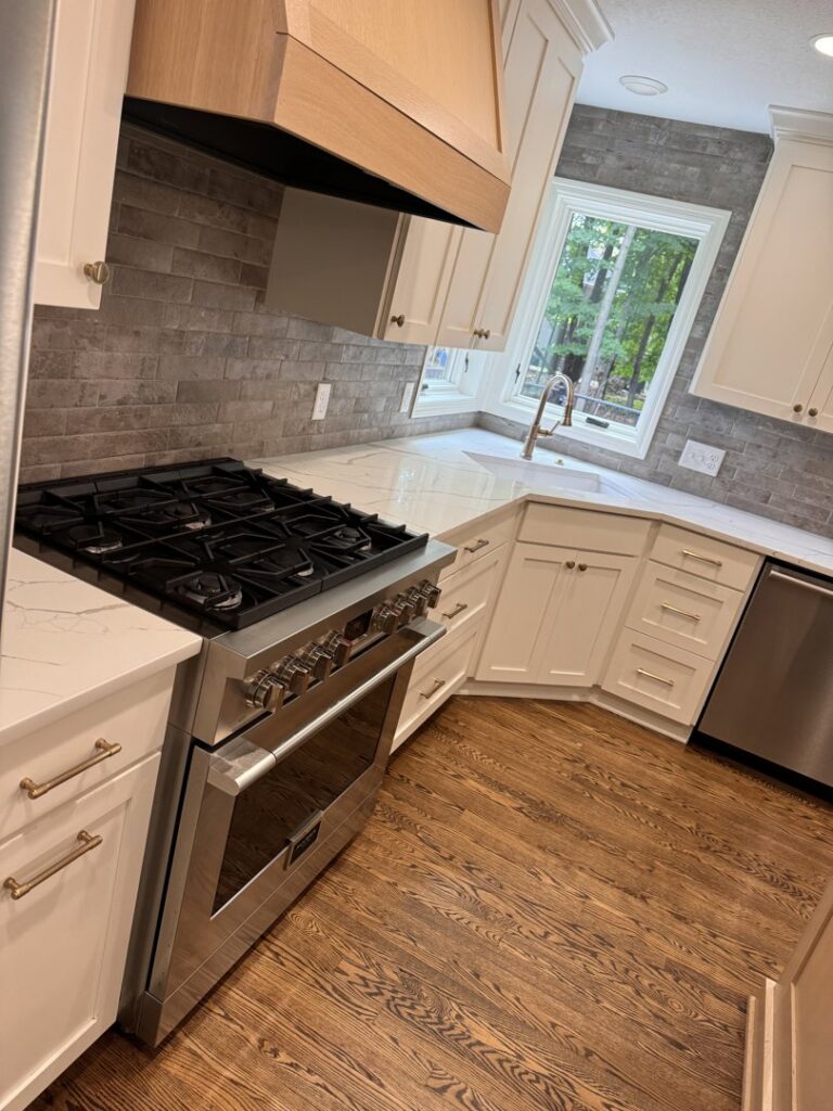 A renovated kitchen featuring white cabinets, a gas range, and a stylish tiled backsplash by Inova Builds in Bloomington, MN.
