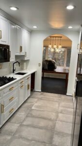 A newly renovated kitchen featuring white cabinets, a black sink, new countertops, and tiled floor by Ruach Home Services in Laurel, MD.