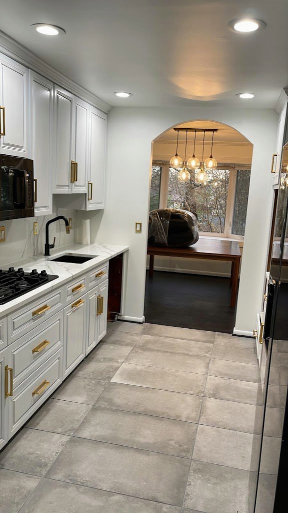 A newly renovated kitchen featuring white cabinets, a black sink, new countertops, and tiled floor by Ruach Home Services in Laurel, MD.