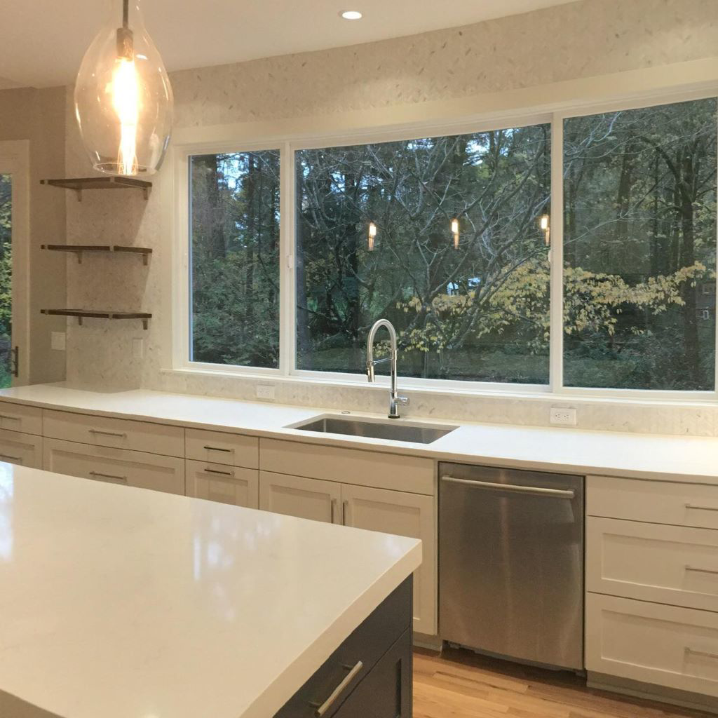 A kitchen sink area with white countertops, large window, and floating shelves installed by Bailey Contracting, LLC in Lake Oswego, OR.