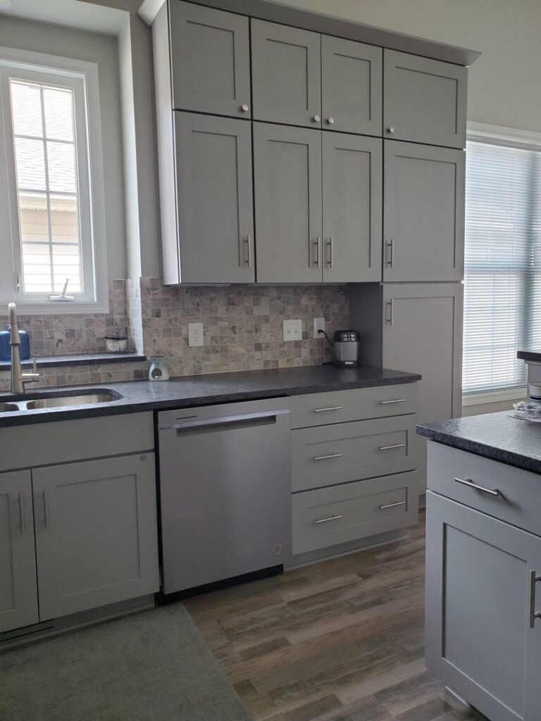 A kitchen sink area with grey cabinets, a mosaic tile backsplash, and a new dishwasher installed by CLE Remodeling Co in Cleveland, OH.