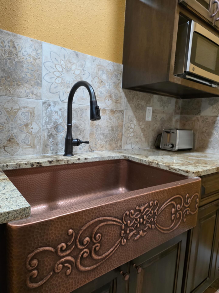 A detailed view of a new copper kitchen sink and decorative tile backsplash by A&R Home Improvements in El Paso, TX