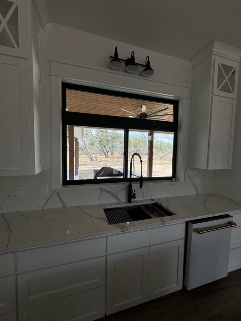 A modern kitchen sink area with white cabinets and quartz countertops, a renovation project by Roaring Lion Renovations, LLC in Houston, TX.