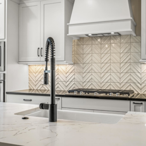 Close-up of a modern kitchen sink, black pull-down faucet, and chevron tile backsplash installed by Mitchco, Inc. in Winston-Salem, NC.