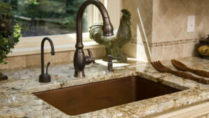 A kitchen sink with a bronze faucet and granite countertop, installed by Surfaces By Design in Duluth, MN.