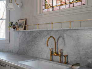 Expert installation of a kitchen sink, brass faucet, and elegant marble backsplash by Tusk Builders in Minneapolis, MN.